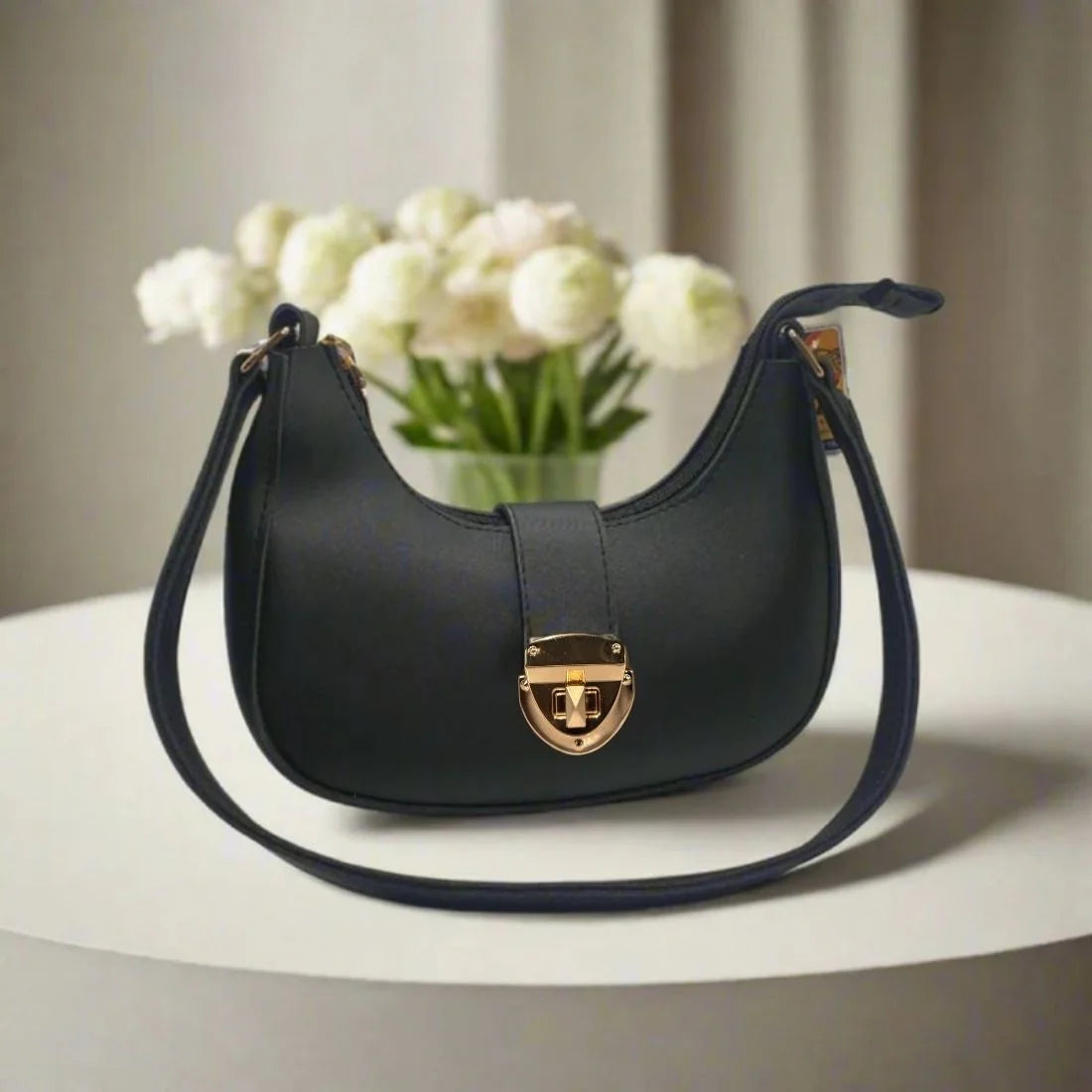 Black handbag with gold clasp on a white surface with white flowers in the background